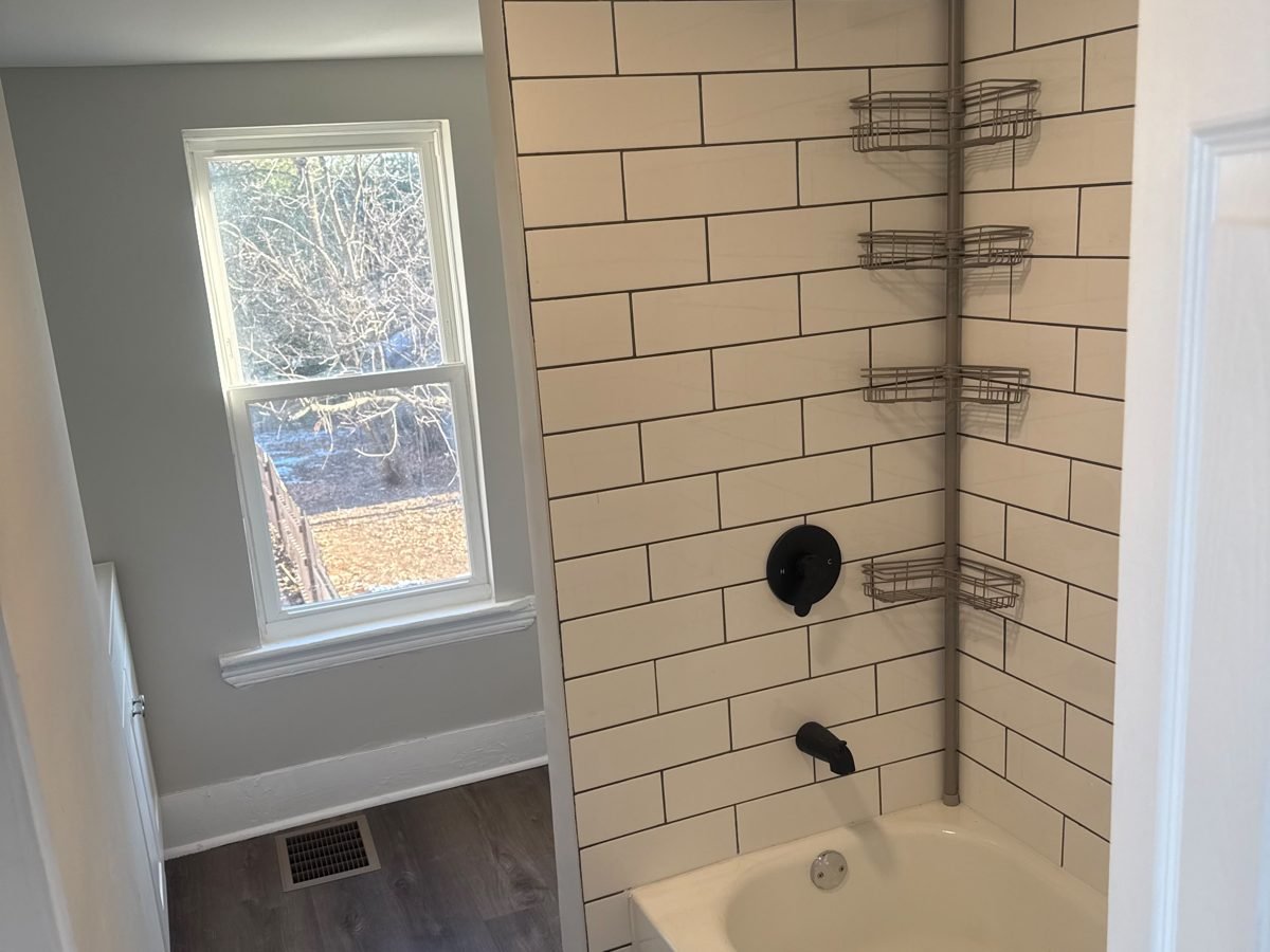 Remodeled bathroom with a white subway-tile tub surround, black fixtures and vinyl plank floor