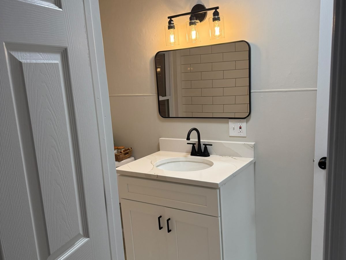 Refreshed bathroom with a white vanity, black-framed mirror, sconce and light tile floor